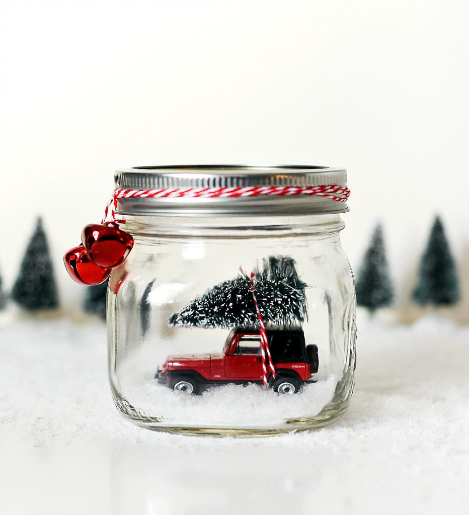 A small car and Christmas tree inside a mason jar snowglobe.