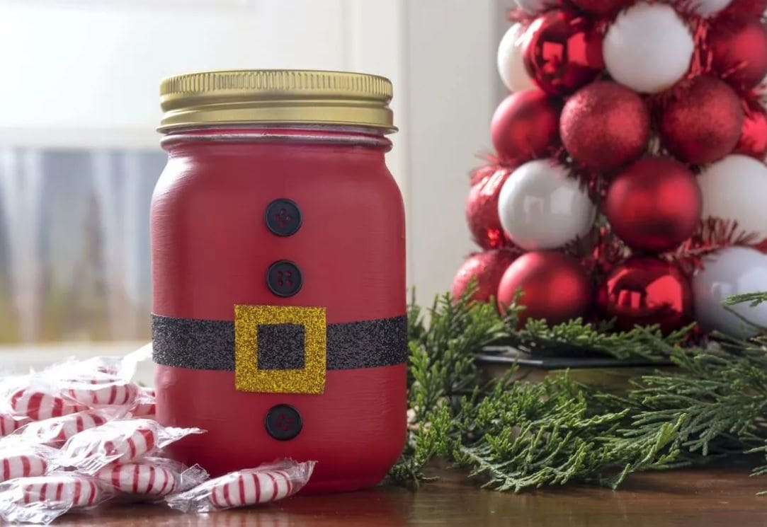 A mason jar painted red and decorated with buttons and a Santa belt.