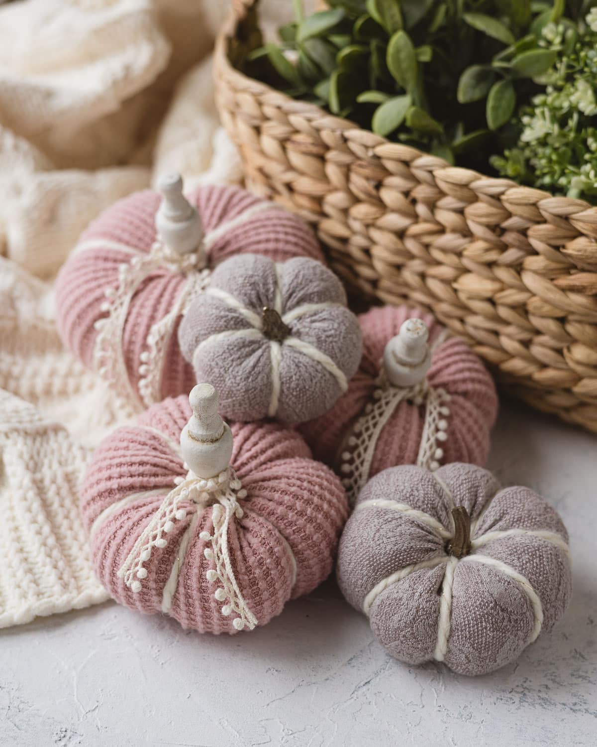 Pink and light purple sweater pumpkins decorated with lace, pumpkin stems, and wooden finial stems.