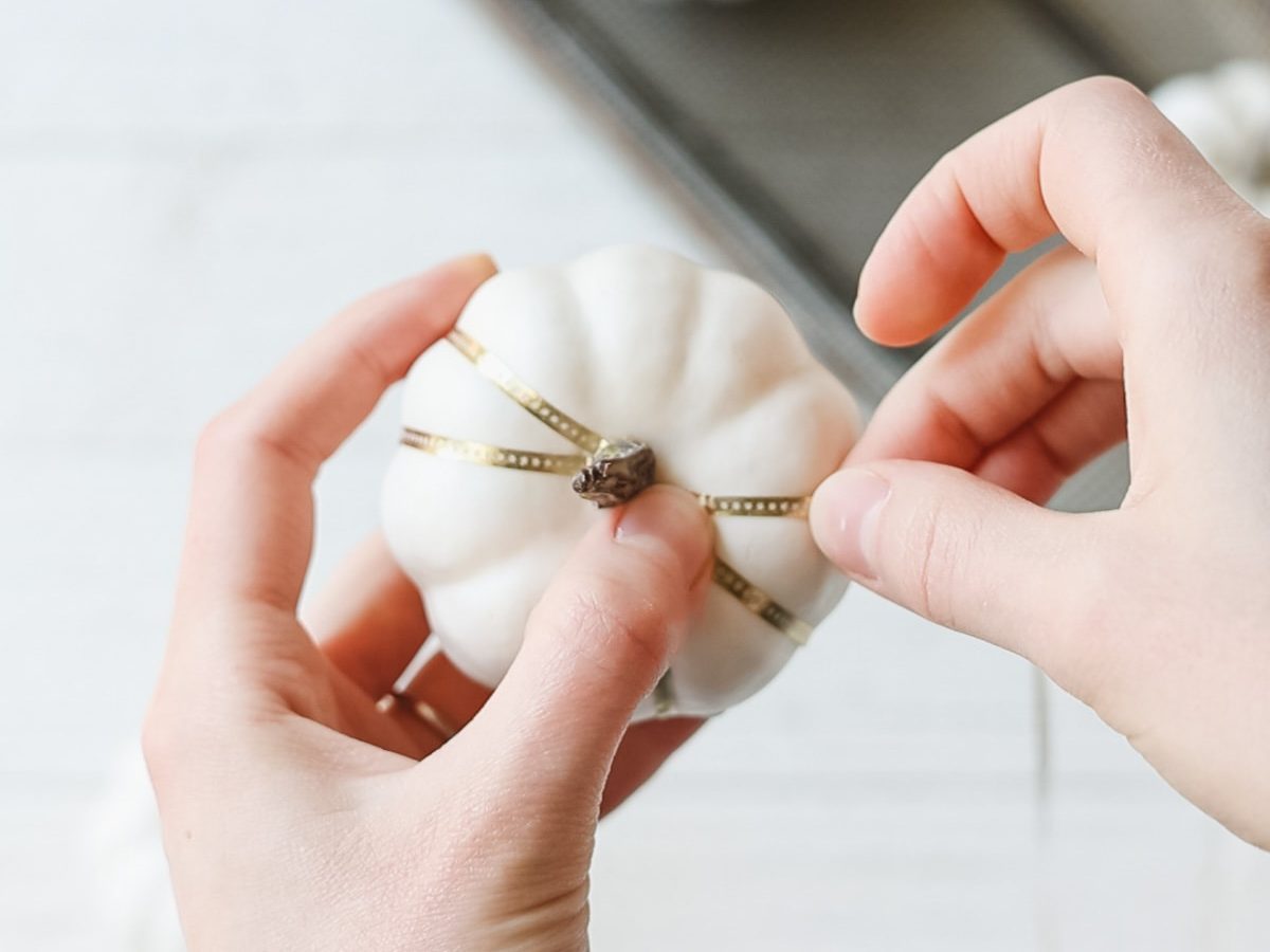 Wrapping gold washi tape around a white foam pumpkin.