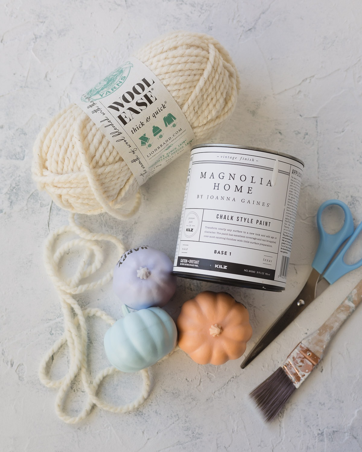 White bulky weight yarn, faux pumpkins, scissors, a paintbrush, and a can of chalk style paint.