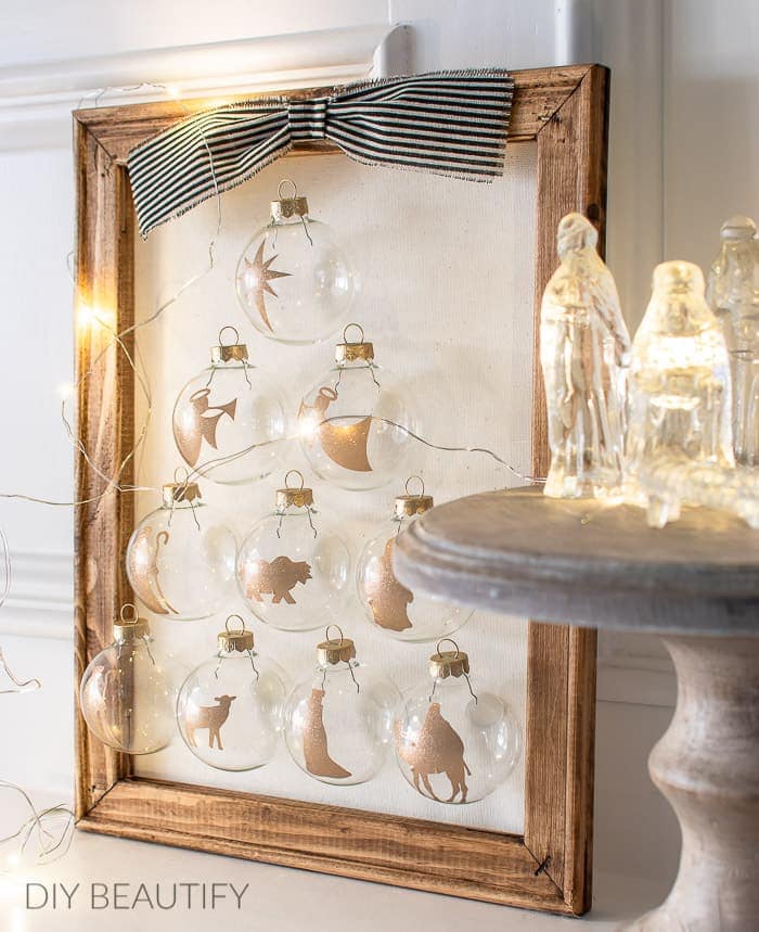 A Christmas Nativity made with clear ornaments, glitter vinyl cutouts and a wooden frame.