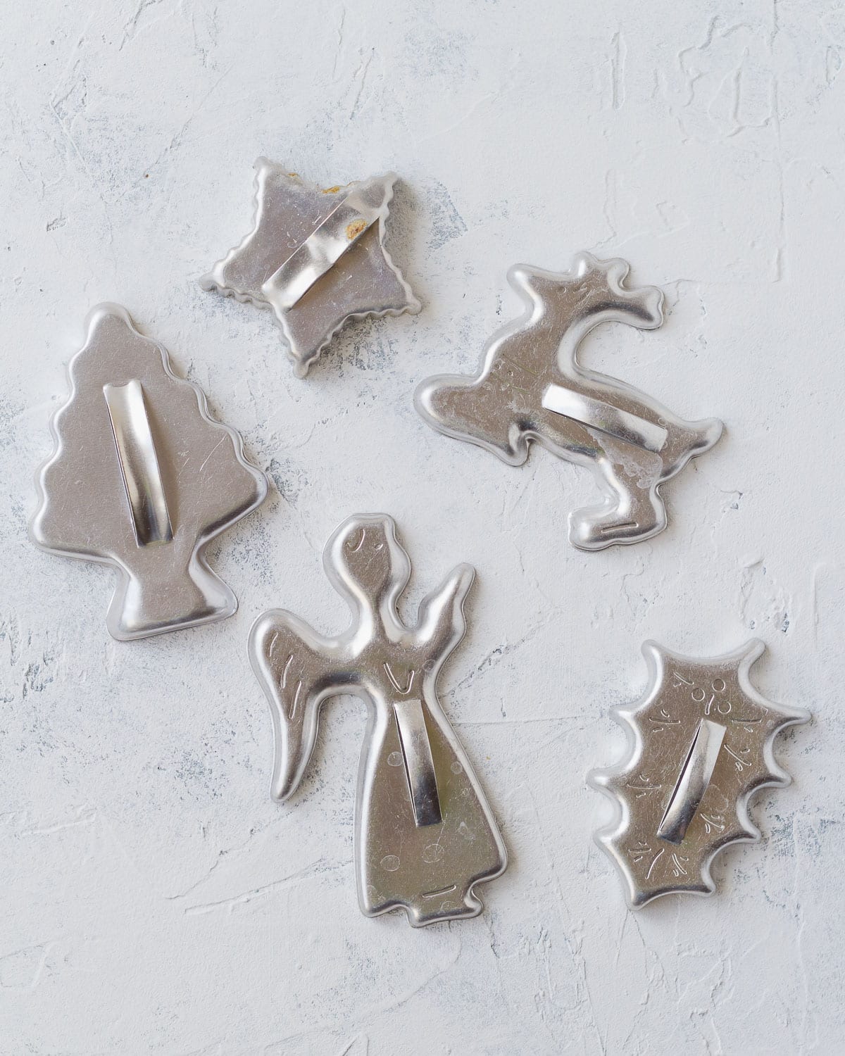 Five vintage metal cookie cutter shapes including an angel, Christmas tree, and reindeer.