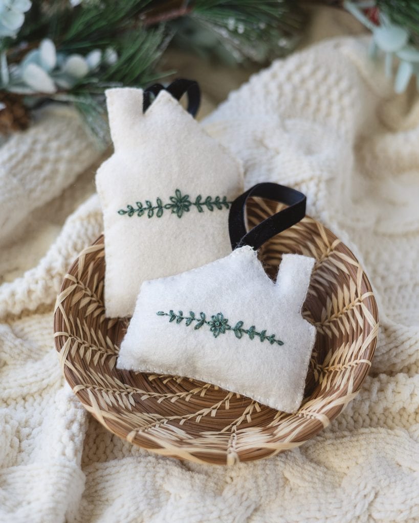 Felt house ornaments with green floral embroidery in a woven basket.