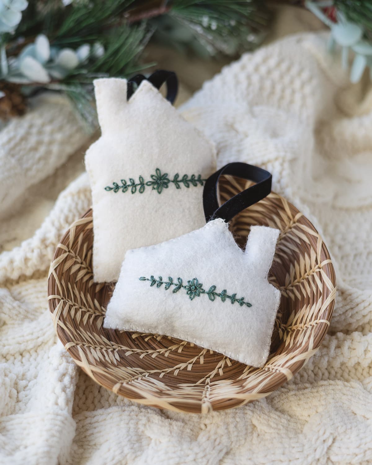 Felt house ornaments with green floral embroidery in a woven basket.