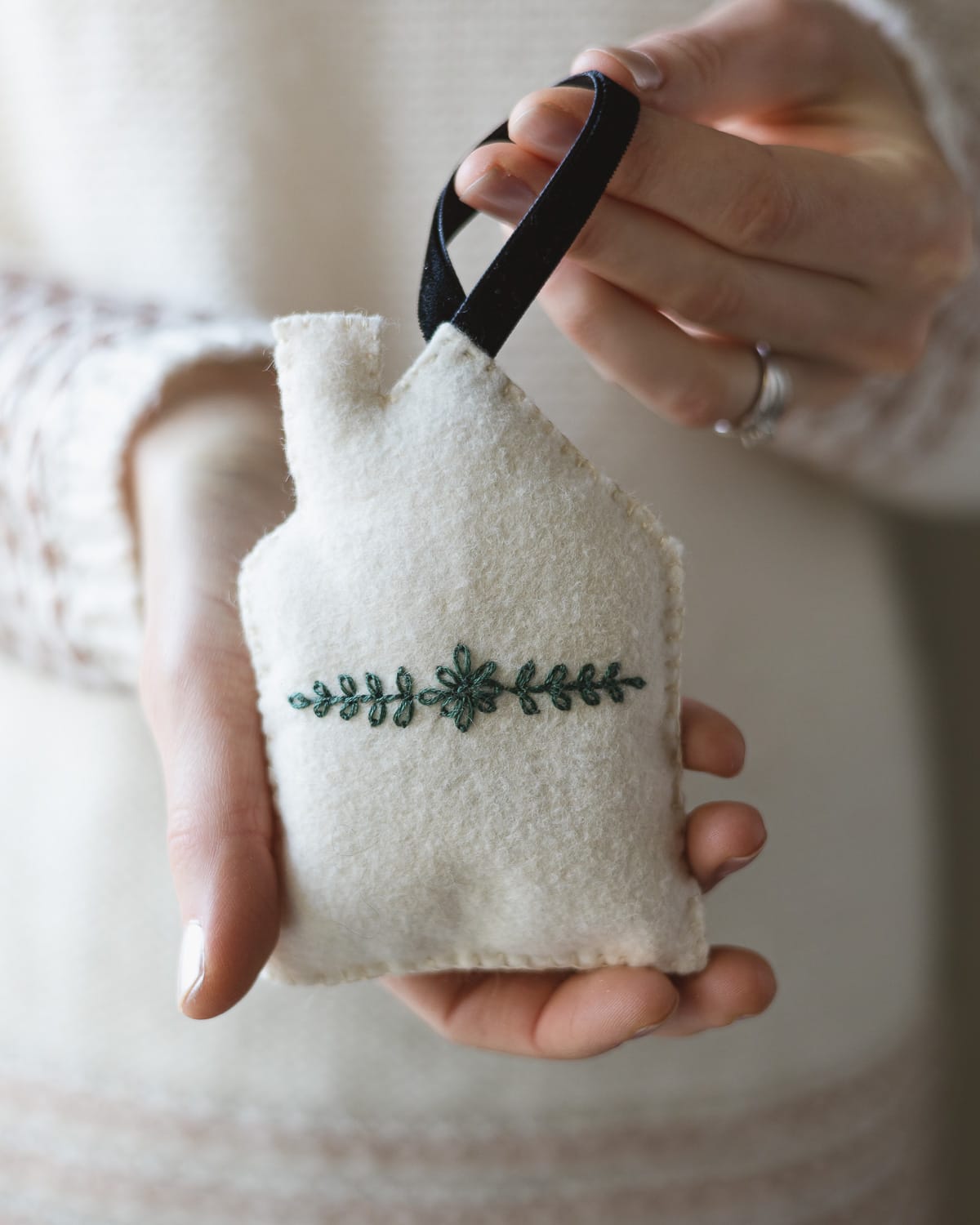 A woman holding a white felt house ornament with green embroidery.