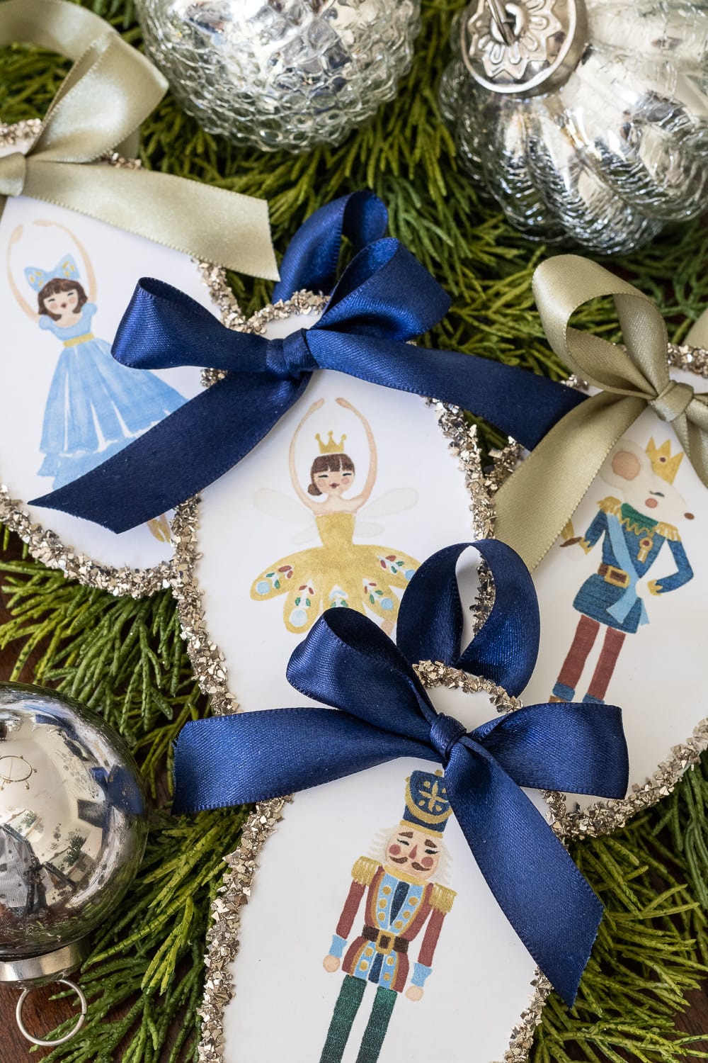 Nutcracker print ornaments with glitter edge and blue ribbons.