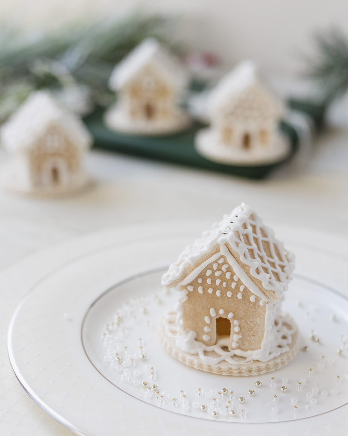 A white salt dough mini gingerbread house on a plate with scattered seed beads.
