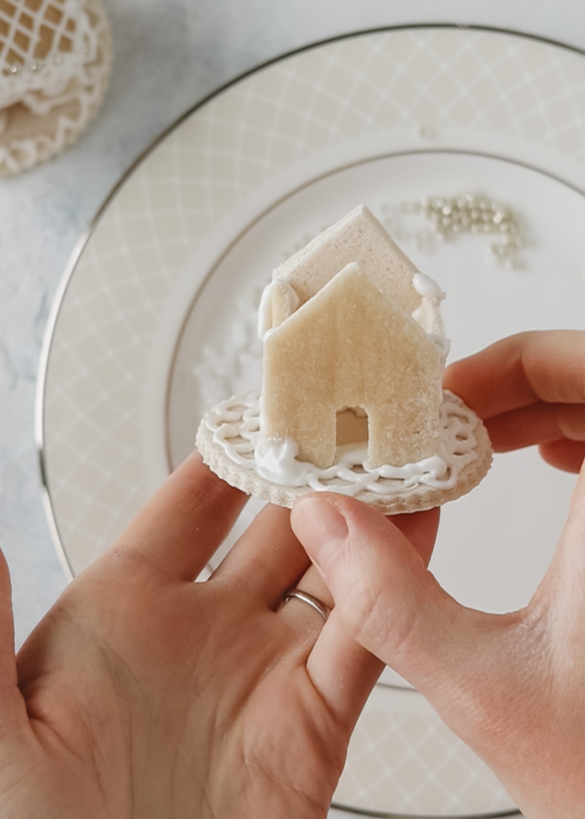 Hands holding a partially constructed mini salt dough gingerbread house.