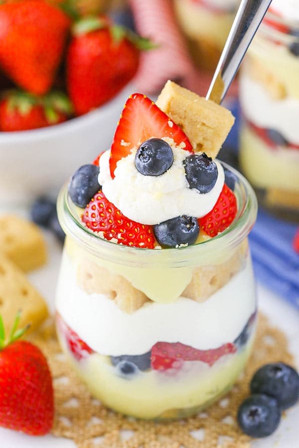 A berry custard trifle in a small glass jar garnished with whipped cream and fresh strawberries and blueberries.