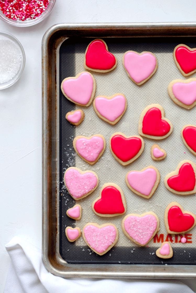 A baking tray of sugar cookie hearts frosted with pink and red frosting.