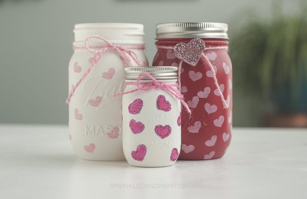 Three mason jars painted and decorated with hearts.