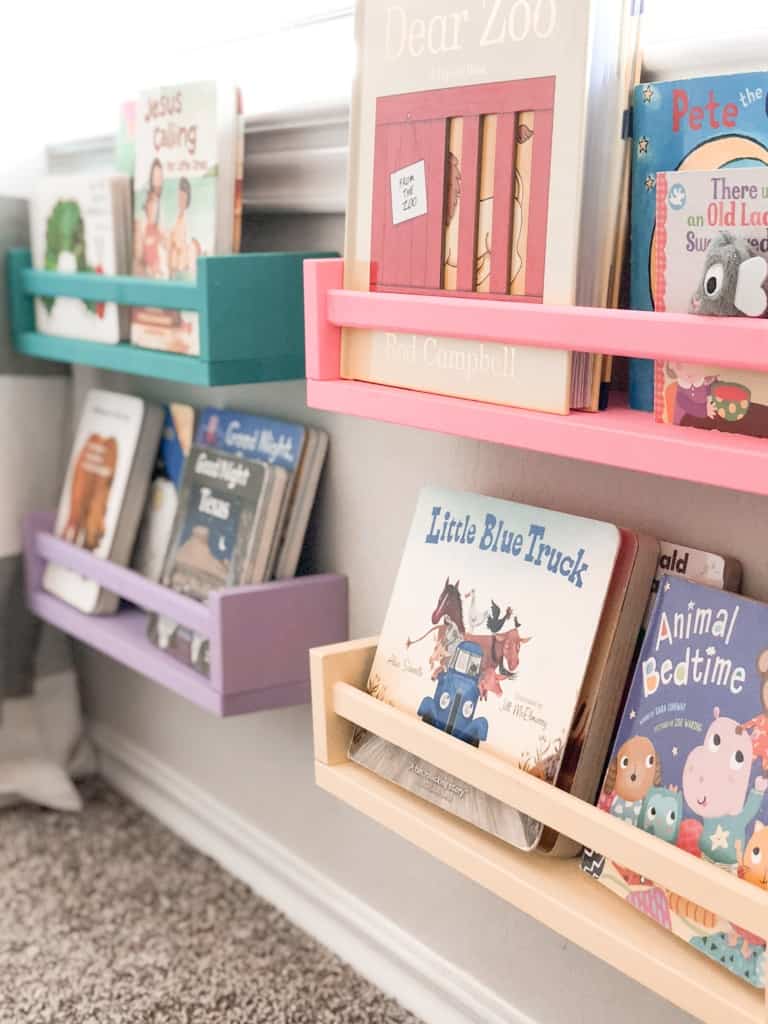 A green, purple, pink, and yellow IKEA spice rack hung on the wall and filled with books.