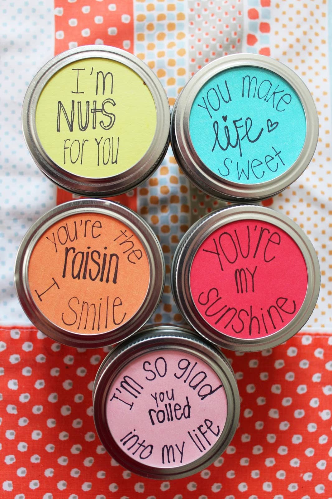 Five mason jar lids with handwritten sayings on each one.