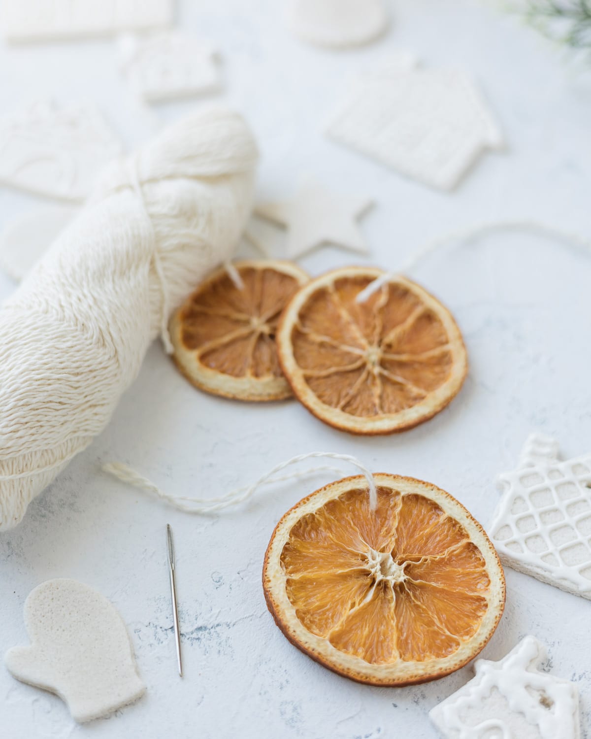 A dried orange slice ornament, needle, and skein of yarn.