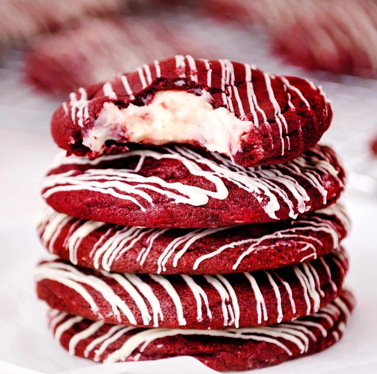 A stack of red velvet cookies stuffed with cream cheese and drizzled with white chocolate.