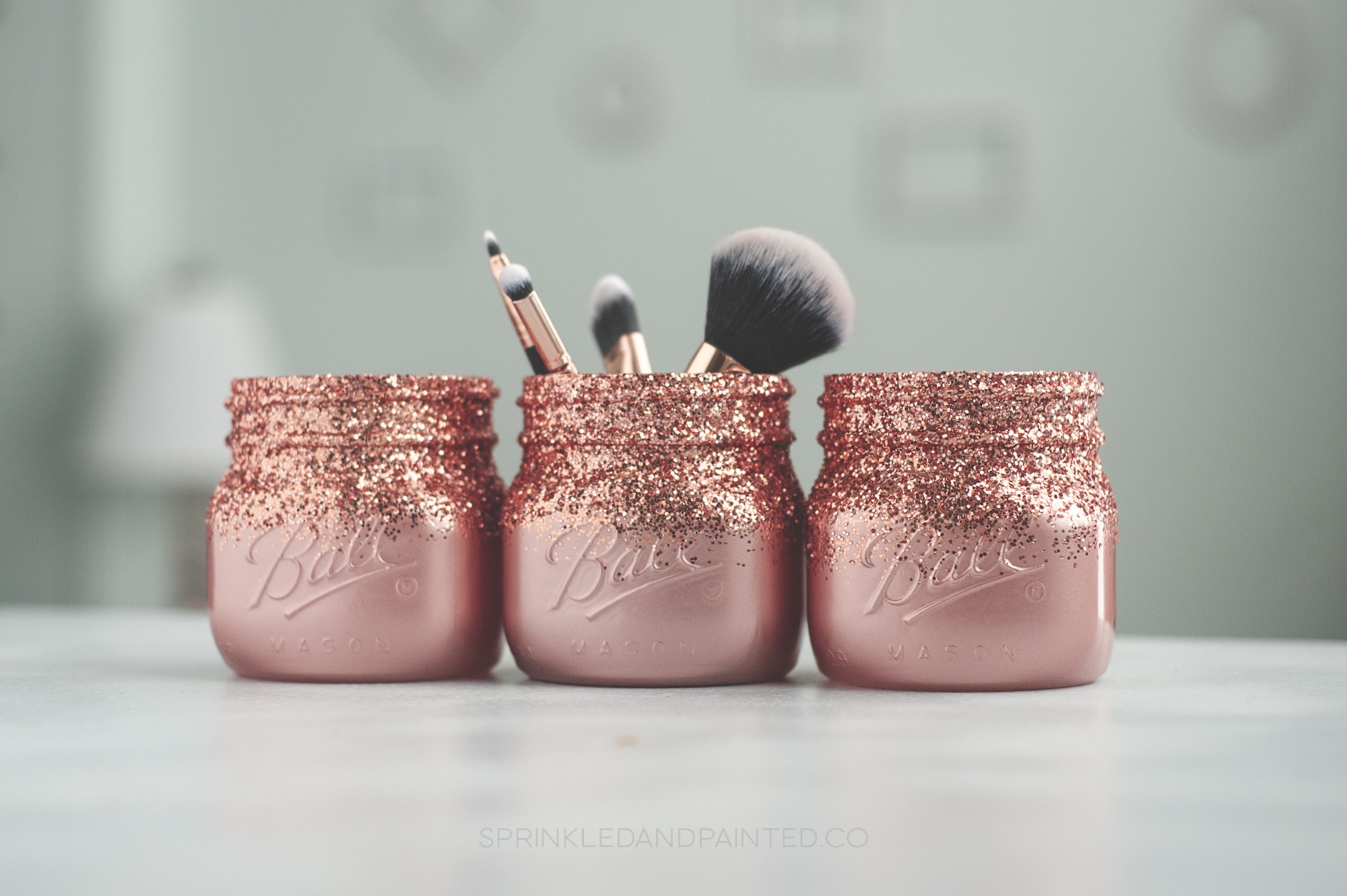 Three rose gold glitter mason jars, one with makeup brushes inside.