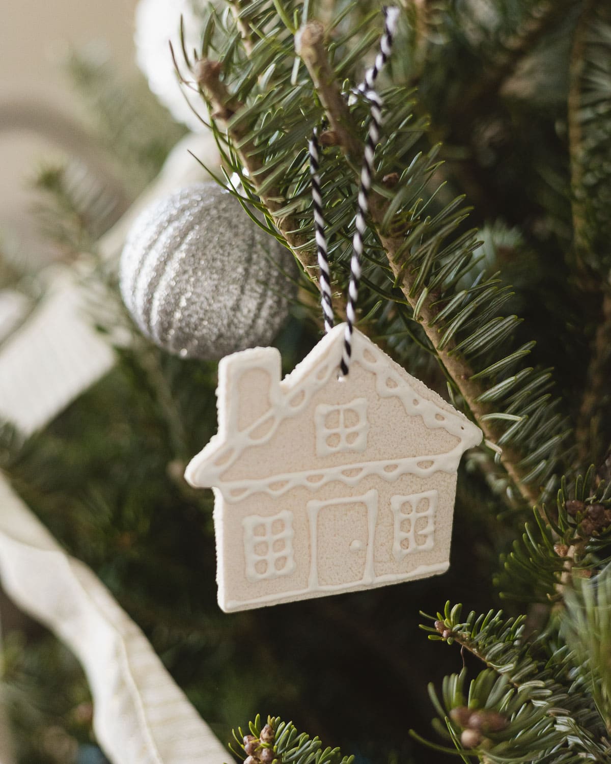 A salt dough ornament cut in the shape of a house hanging on a pine tree.