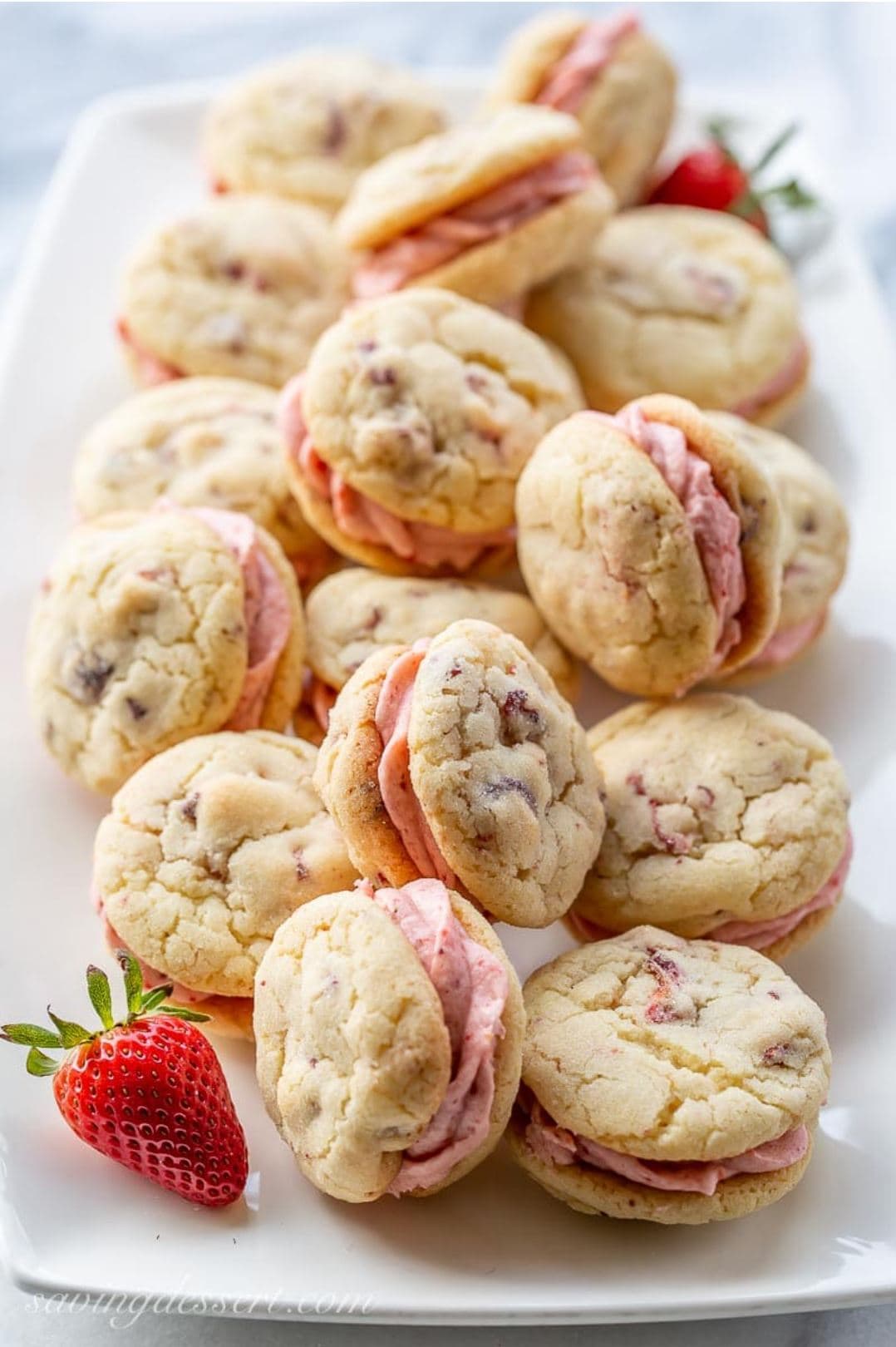 Strawberry sandwich cookies with strawberry buttercream on a white platter.