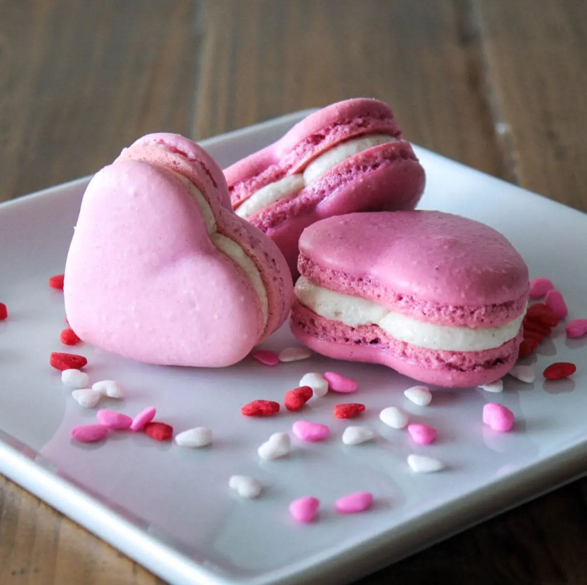 Three Valentine Heart Macarons and heart-shaped sprinkles on a white plate.