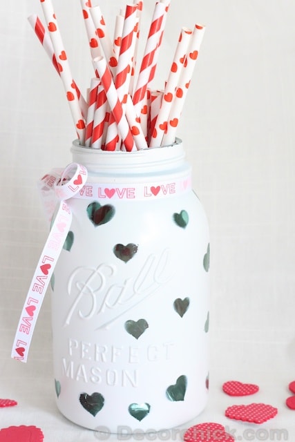 A mason jar painted white with heart cutouts.