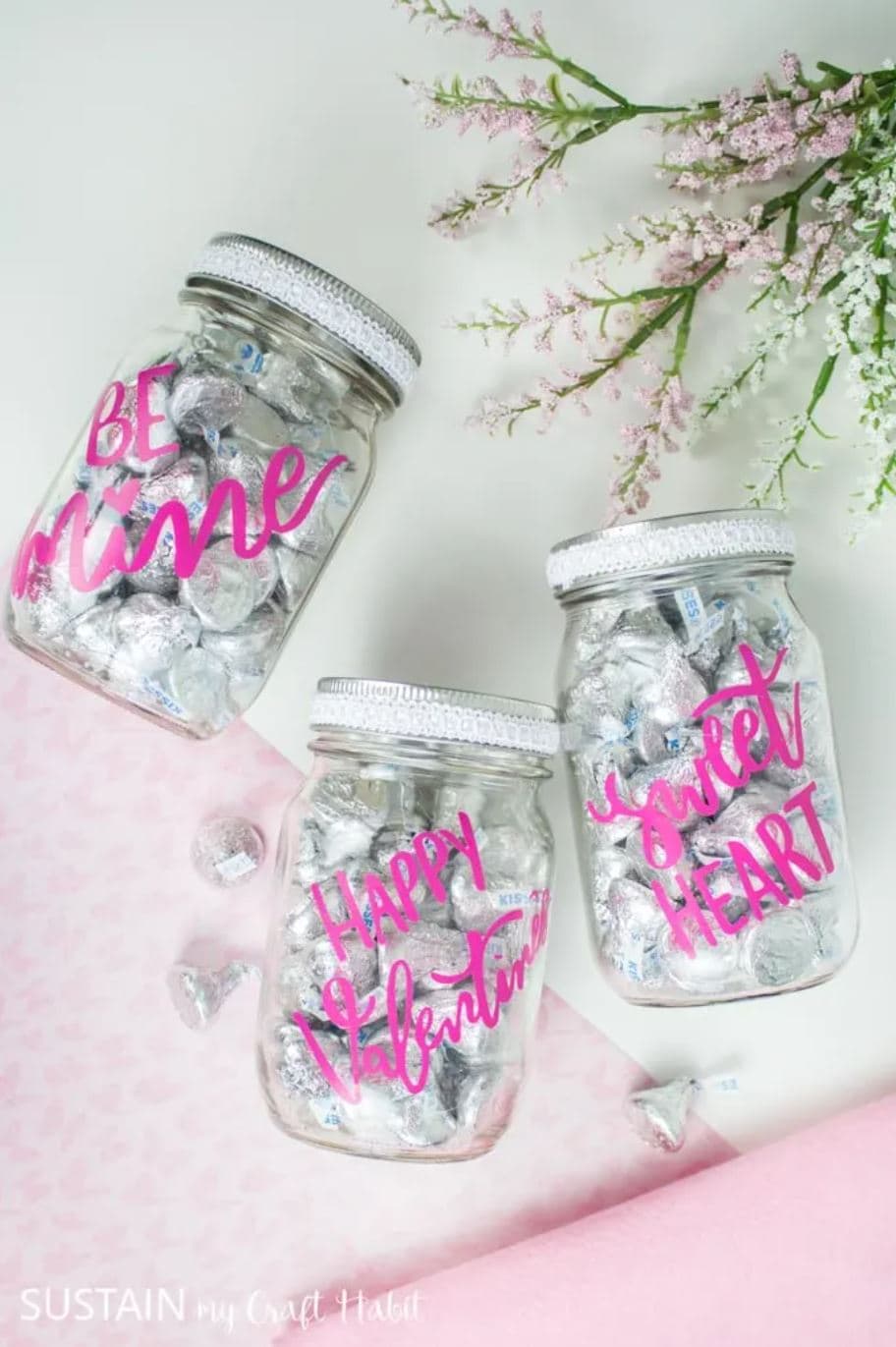 Three mason jars filled with candy and decorated with pink vinyl sayings.