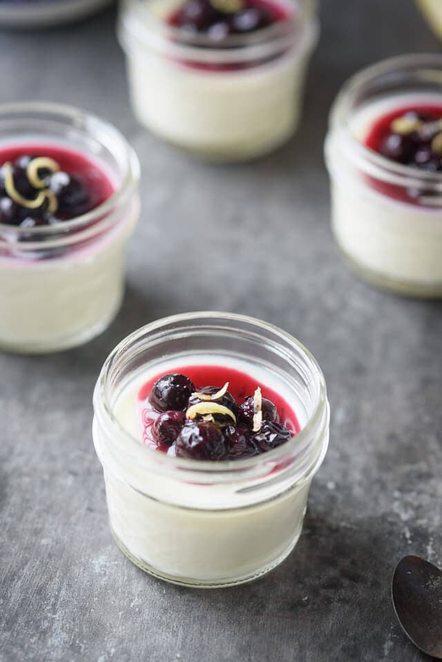 Small jelly jars filled with vanilla panna cotta and topped with a fruit sauce.