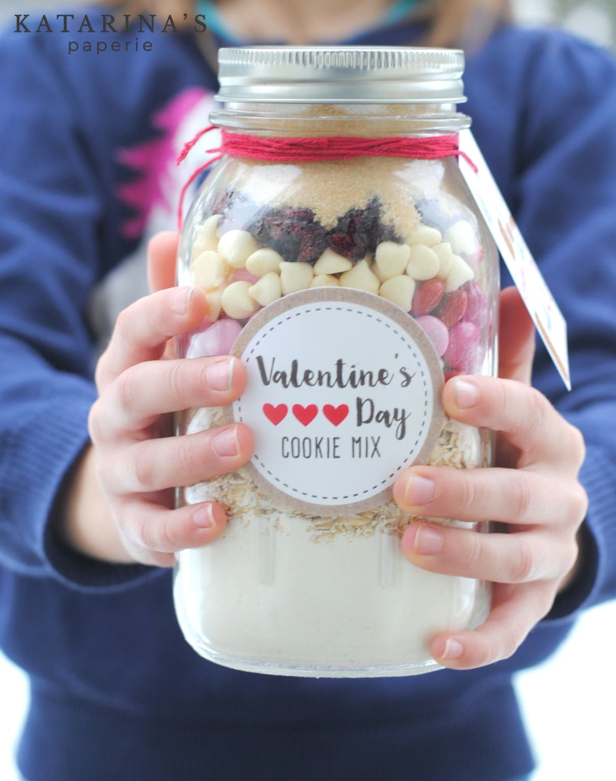 Hands holding a mason jar of Valentine's cookie mix.