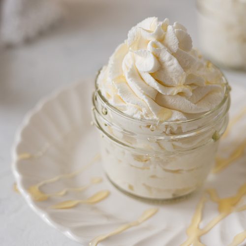 A jar overflowing with piped honey whipped cream and drizzled with honey.