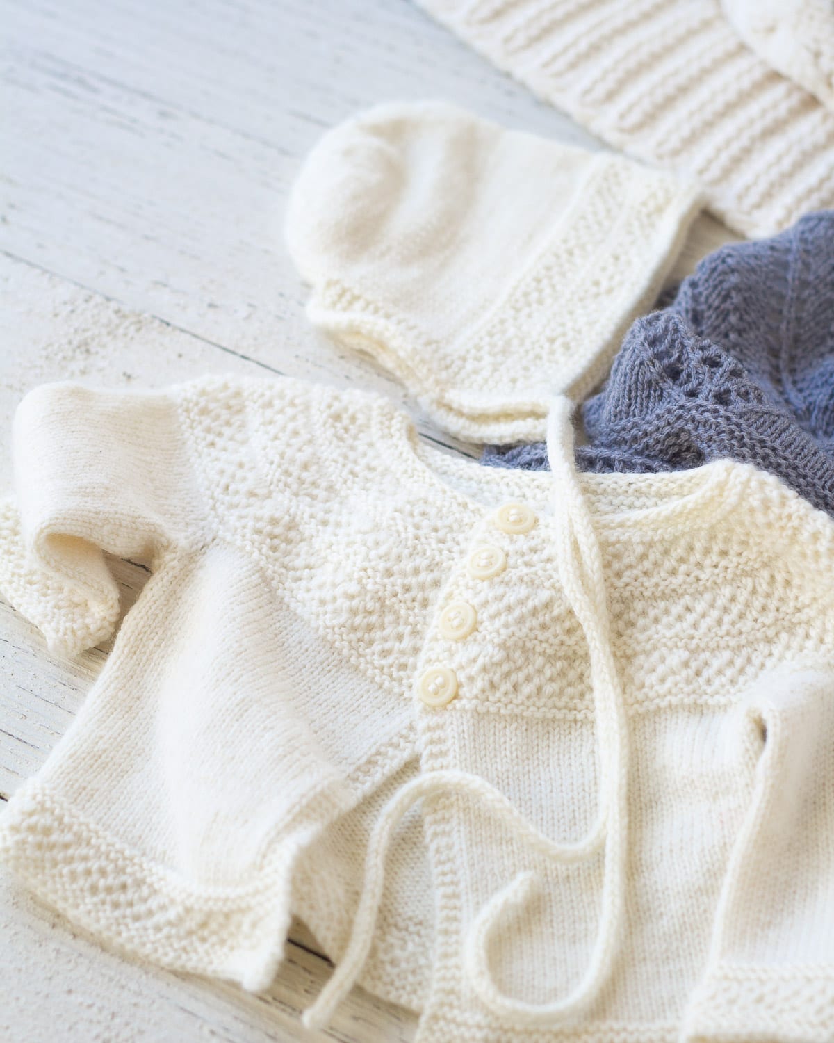 A handknit baby sweater and bonnet in cream yarn.