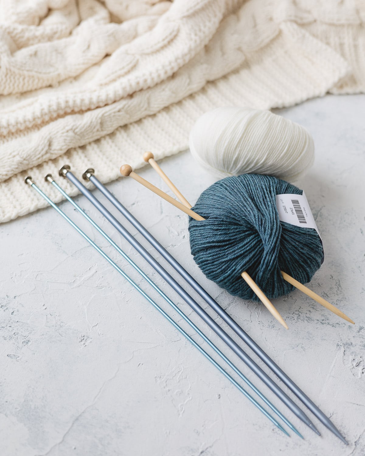 Straight wooden knitting needles in a ball of blue yarn with more straight needles nearby.