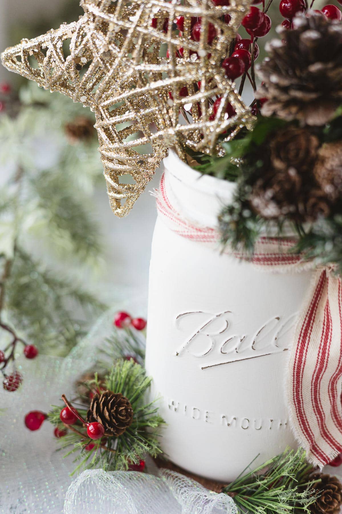 A mason jar decorated for Christmas with red ribbon and greenery.