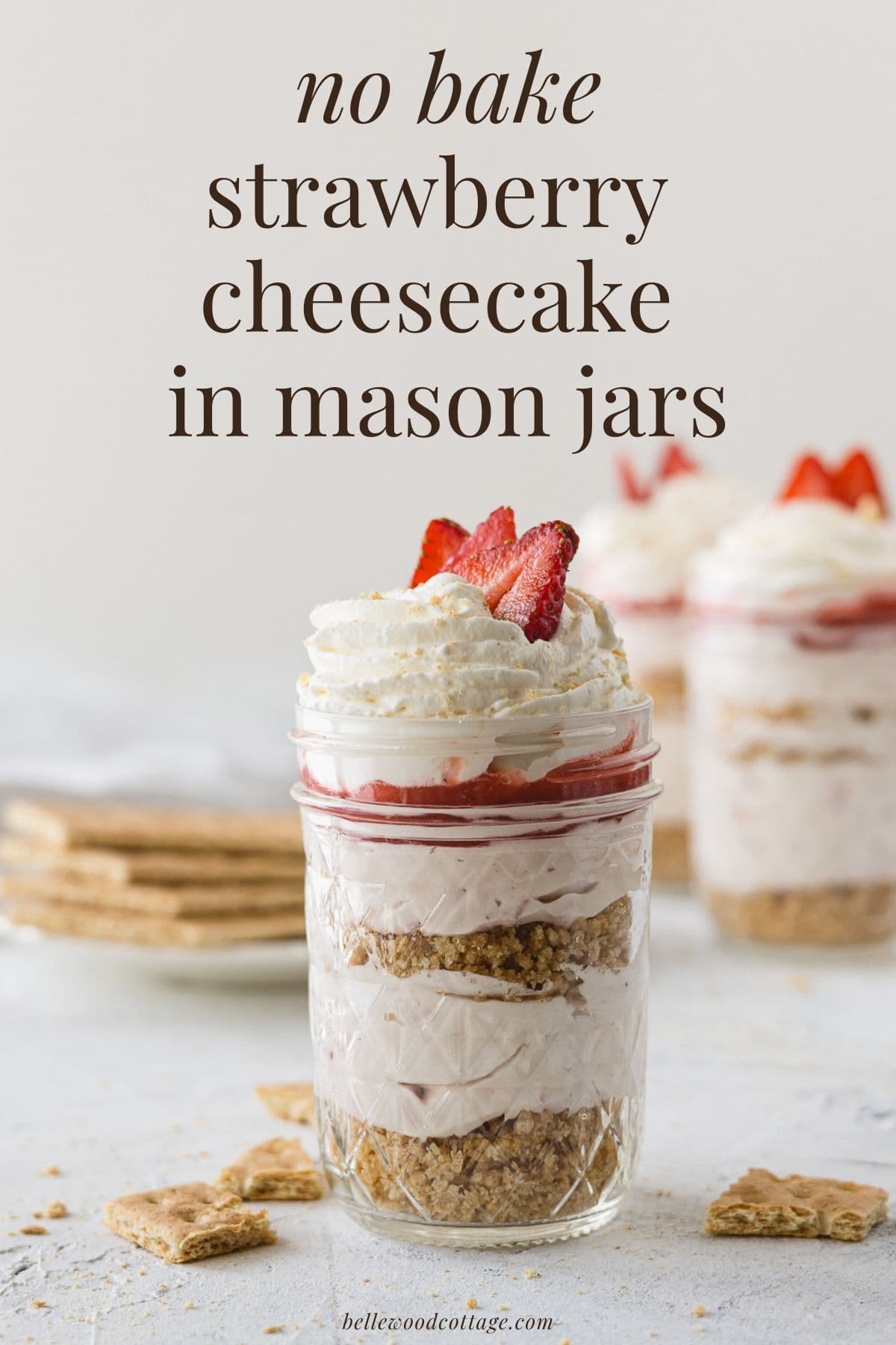 A layered strawberry cheesecake in a jar with the words, "No Bake Strawberry Cheesecakes in Mason Jars".