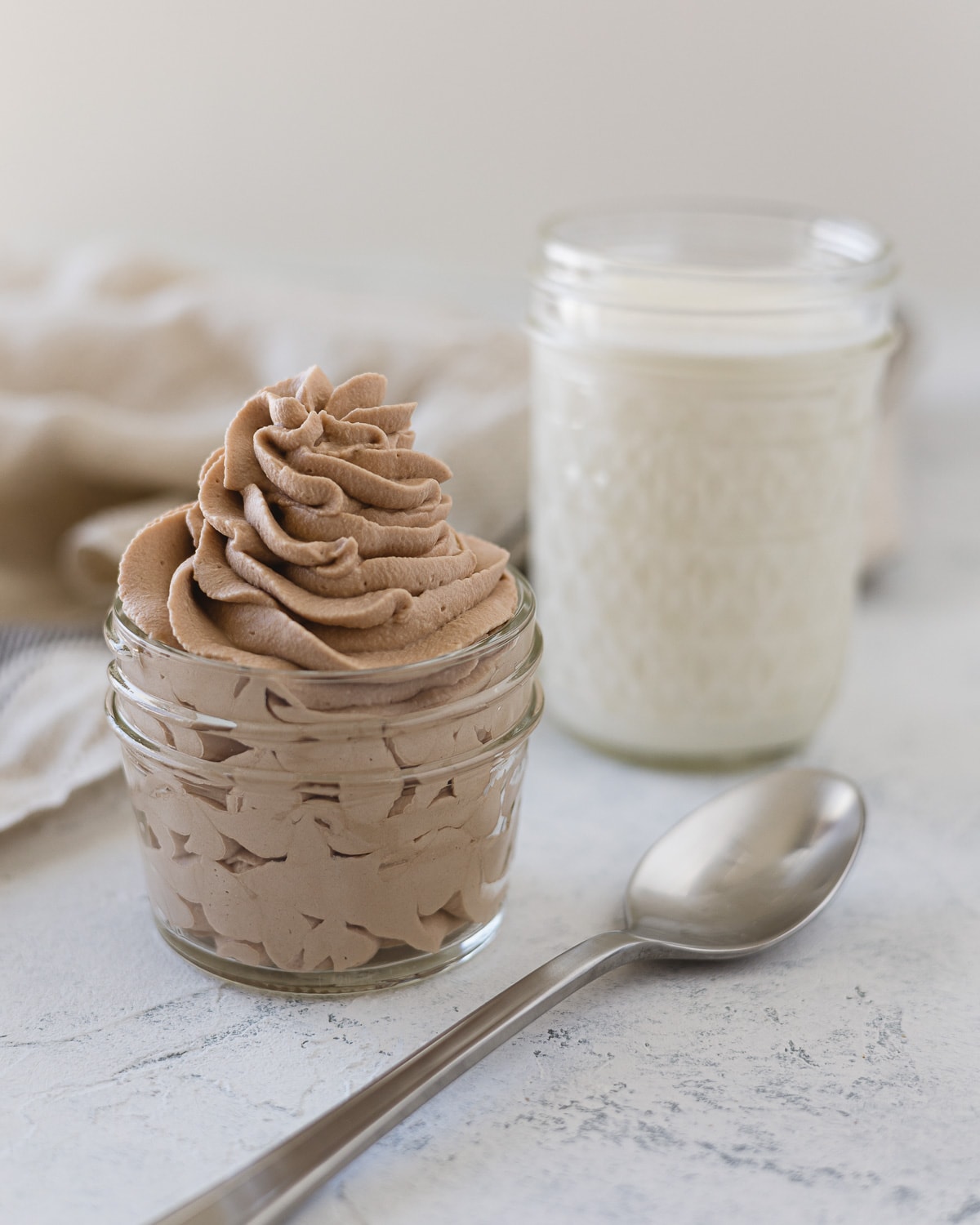 A spoon, mason jar of homemade whipped cream, and a glass of heavy whipping cream.