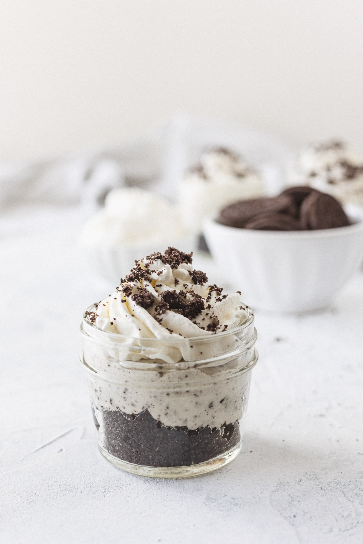 A no bake Oreo cheesecake in a jar topped with whipped cream and crushed Oreos.
