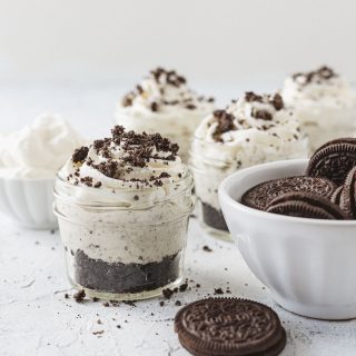 Oreo cheesecakes in small mason jars and a bowl of chocolate sandwich cookies.