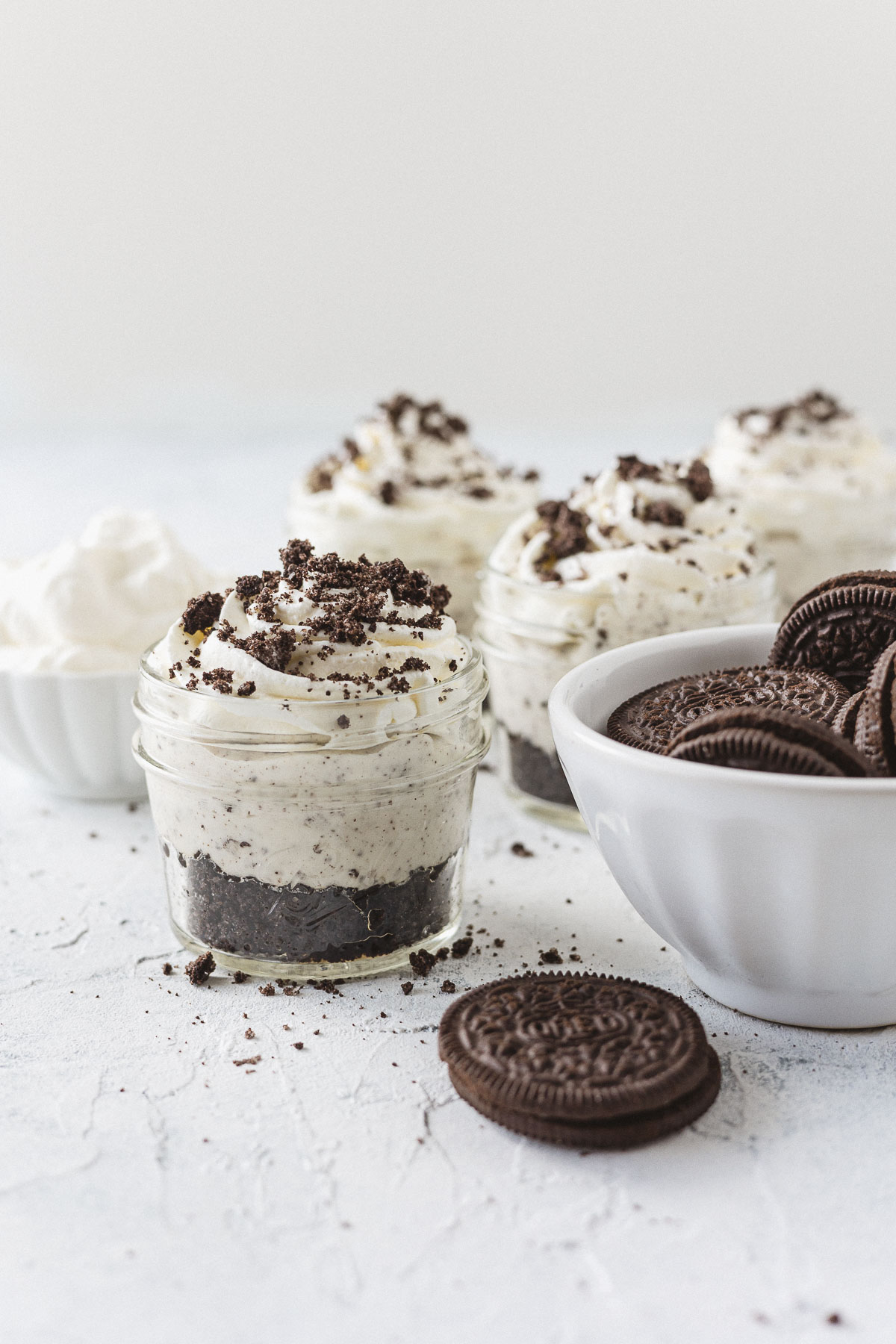 Oreo cheesecakes in small mason jars and a bowl of chocolate sandwich cookies.