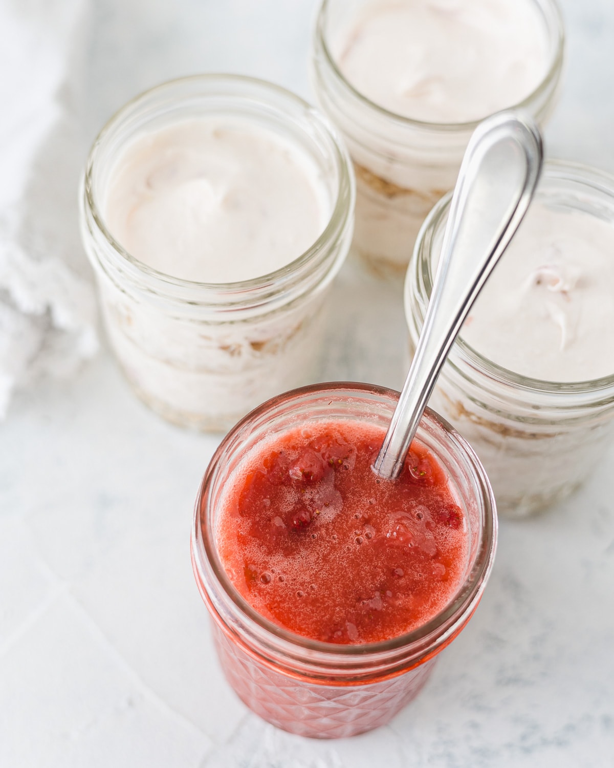 A jar of strawberry sauce and more jars filled with strawberry cheesecake.