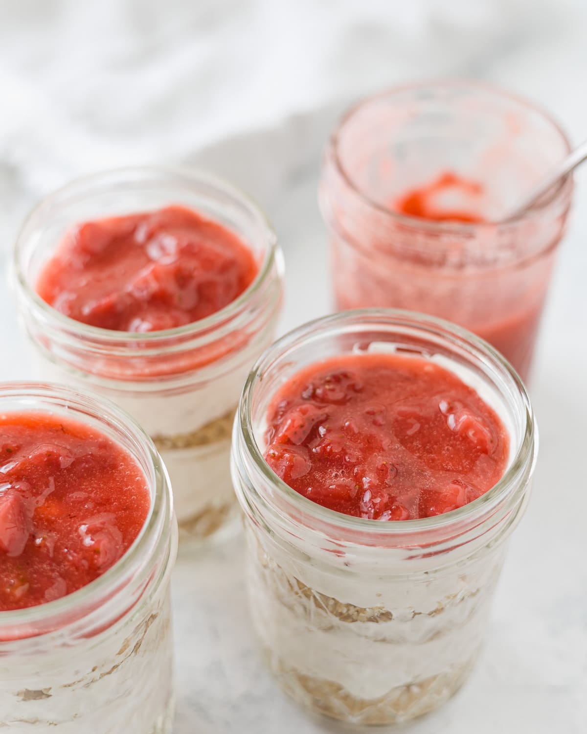 Jars of no bake cheesecake topped with homemade strawberry sauce.