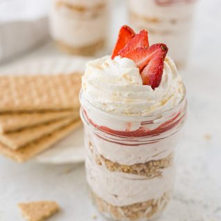 Layered no bake strawberry cheesecake in a mason jar topped with whipped cream and strawberries.