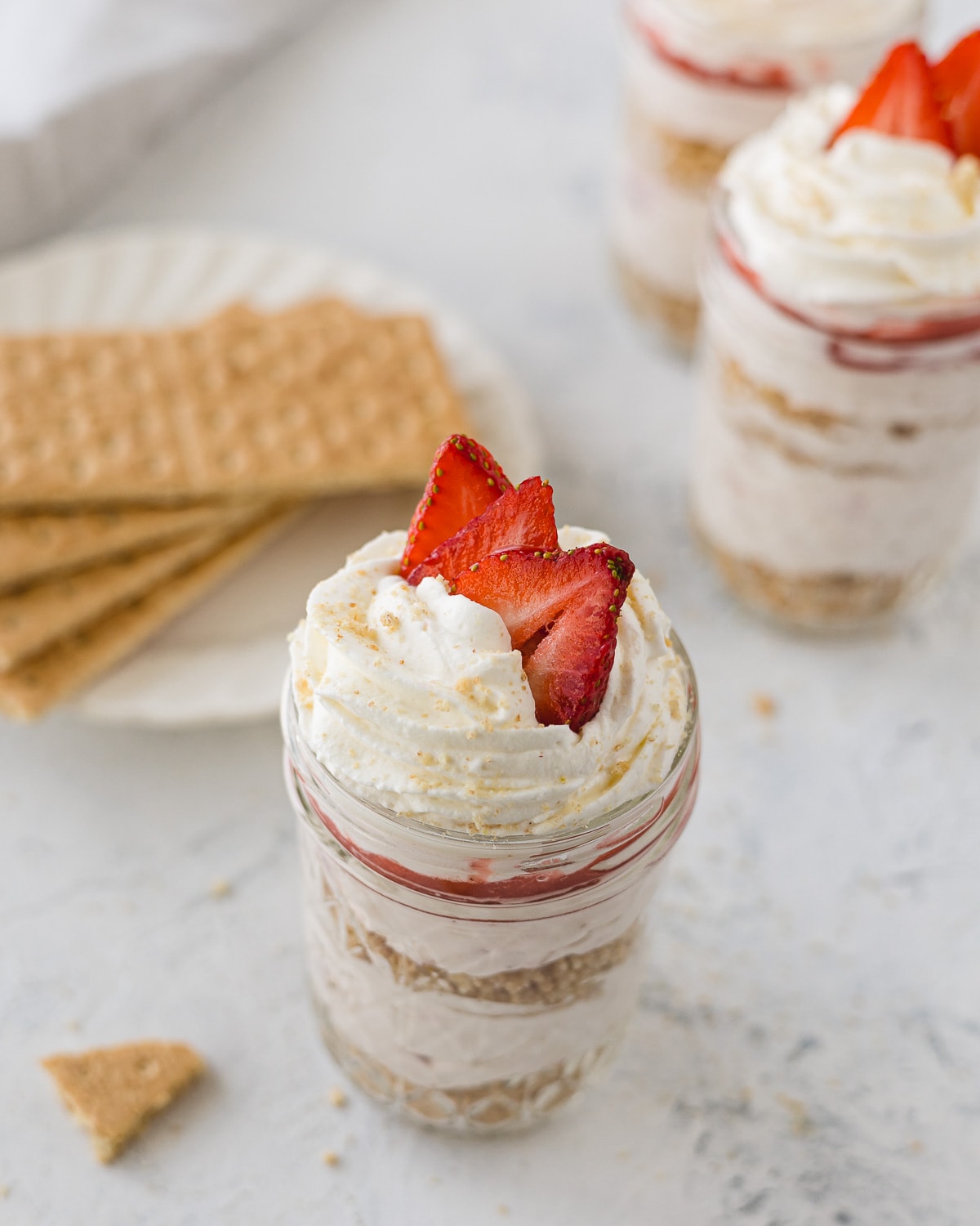 Layered no bake strawberry cheesecake in a mason jar topped with whipped cream and strawberries.