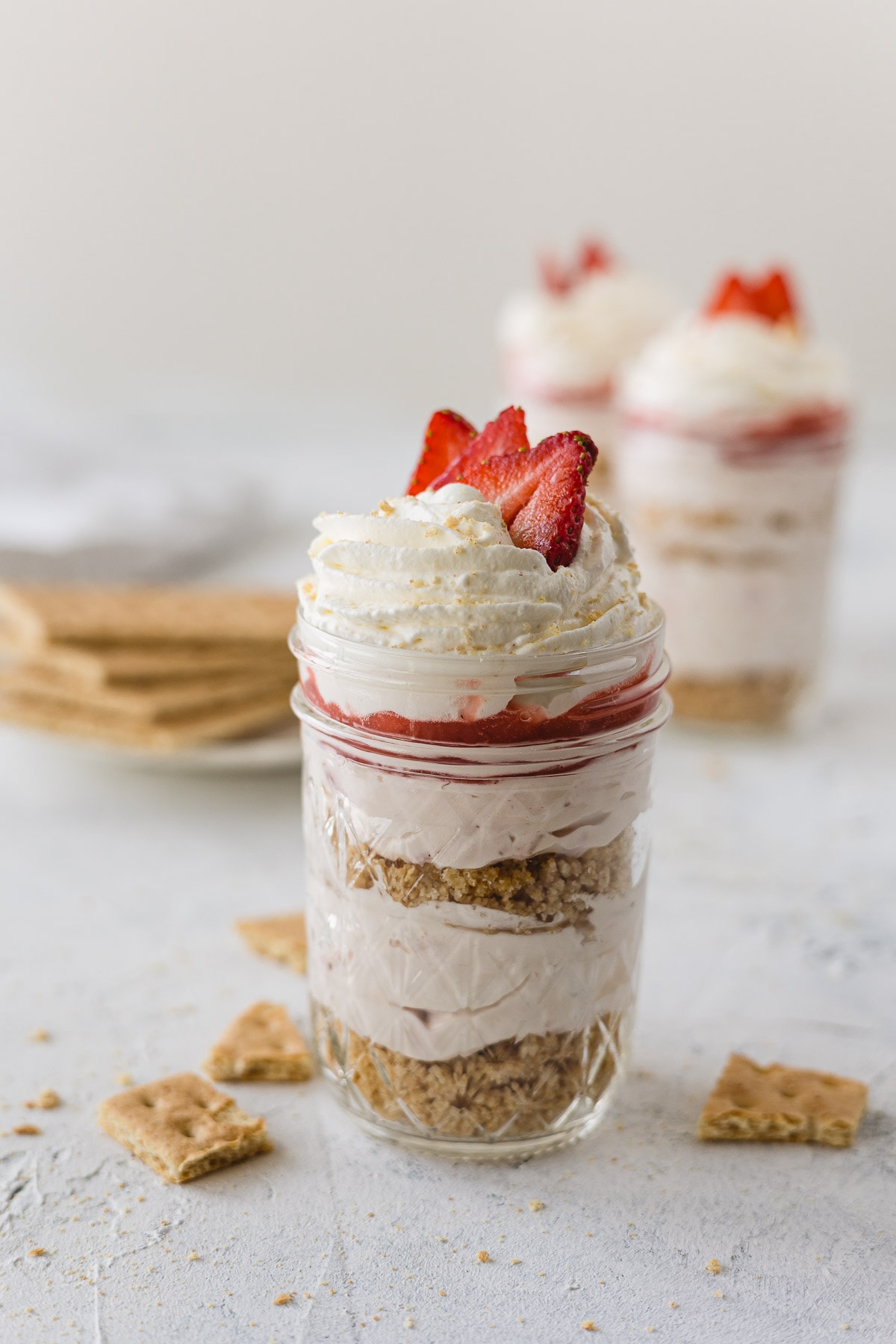 Layered no bake strawberry cheesecake in a mason jar topped with whipped cream and strawberries.