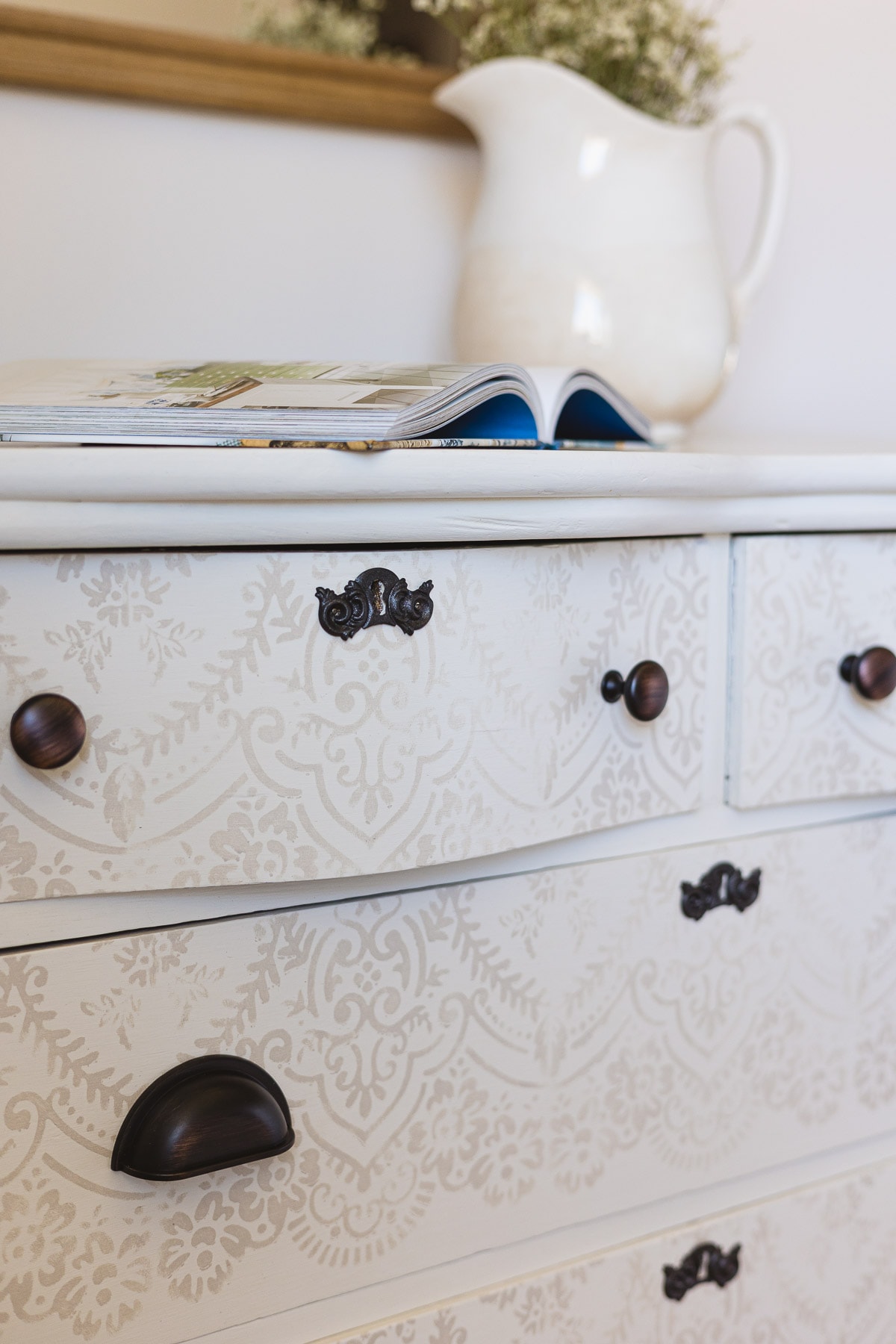 An open book on top of a white painted and stenciled dresser.