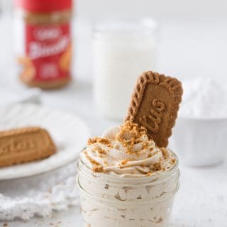 Cookie butter whipped cream piped into a small mason jar with a Biscoff cookie and crumbs on top.