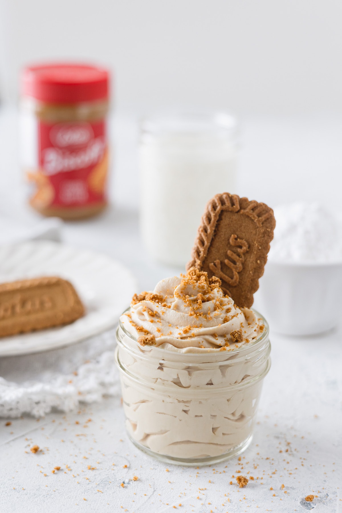 Cookie butter whipped cream piped into a small mason jar with a Biscoff cookie and crumbs on top.