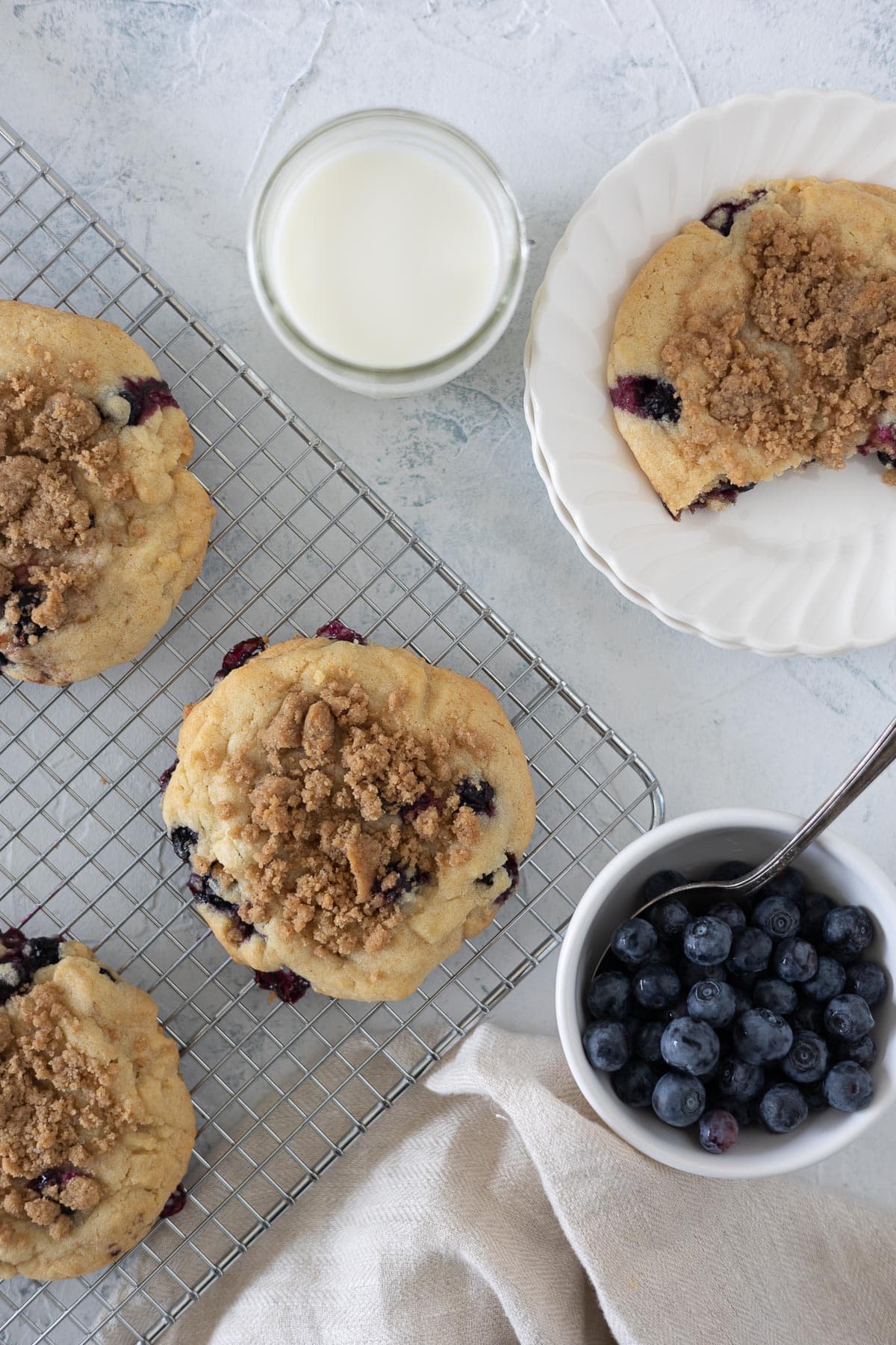 Streusel-topped blueberry cookies on a baking sheet with a small bowl of fresh blueberries.