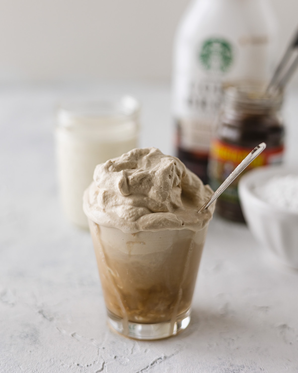 A spoon in a small glass of coffee topped with a scoop of coffee-flavored whipped cream.