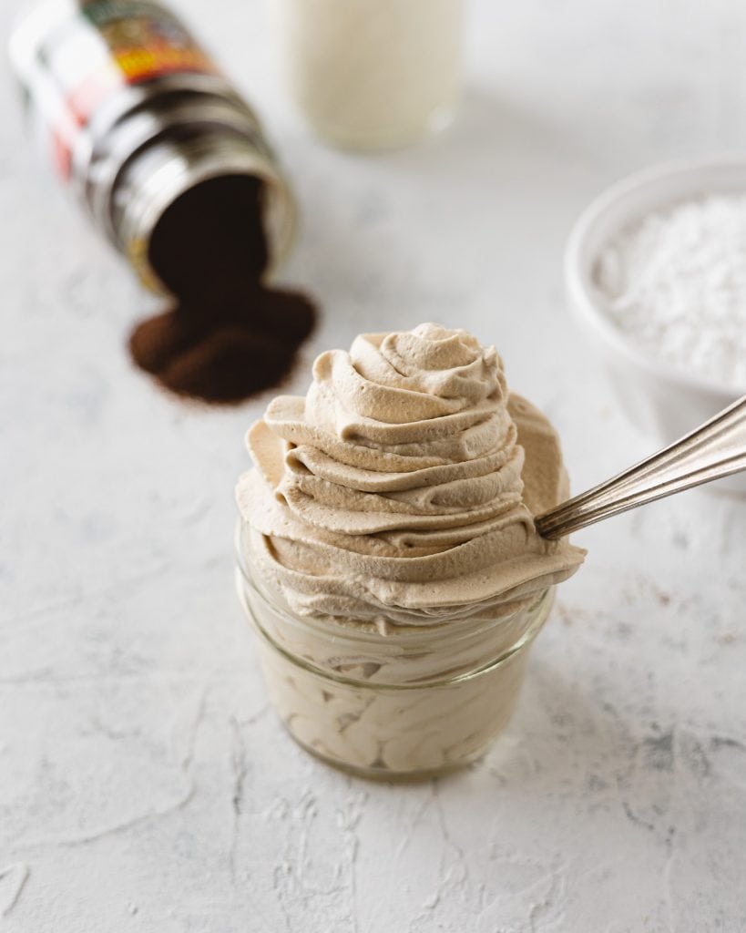 A mason jar filled with piped coffee whipped cream and a spoon.