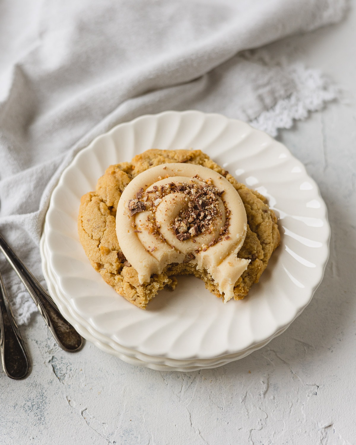 A Peanut Butter Snickers Crumbl Cookie with a bite removed on a small stack of scalloped plates.