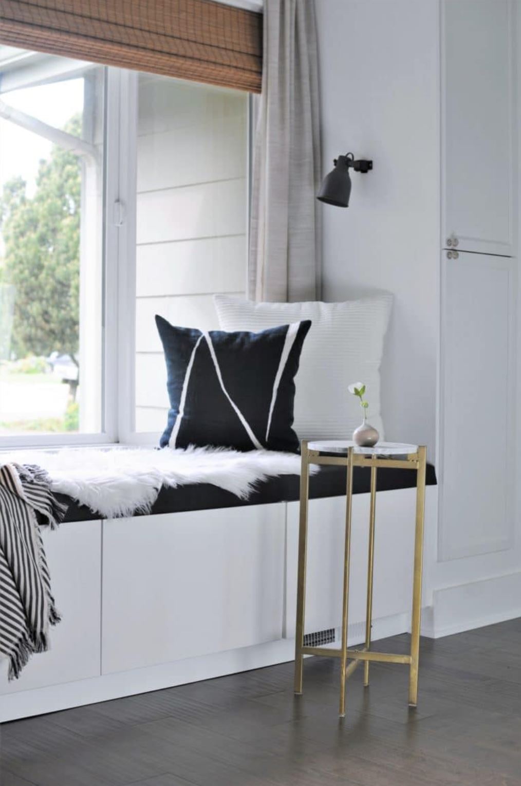 A window seat from IKEA cabinets with cushions, pillows, and an adjacent gold end table.